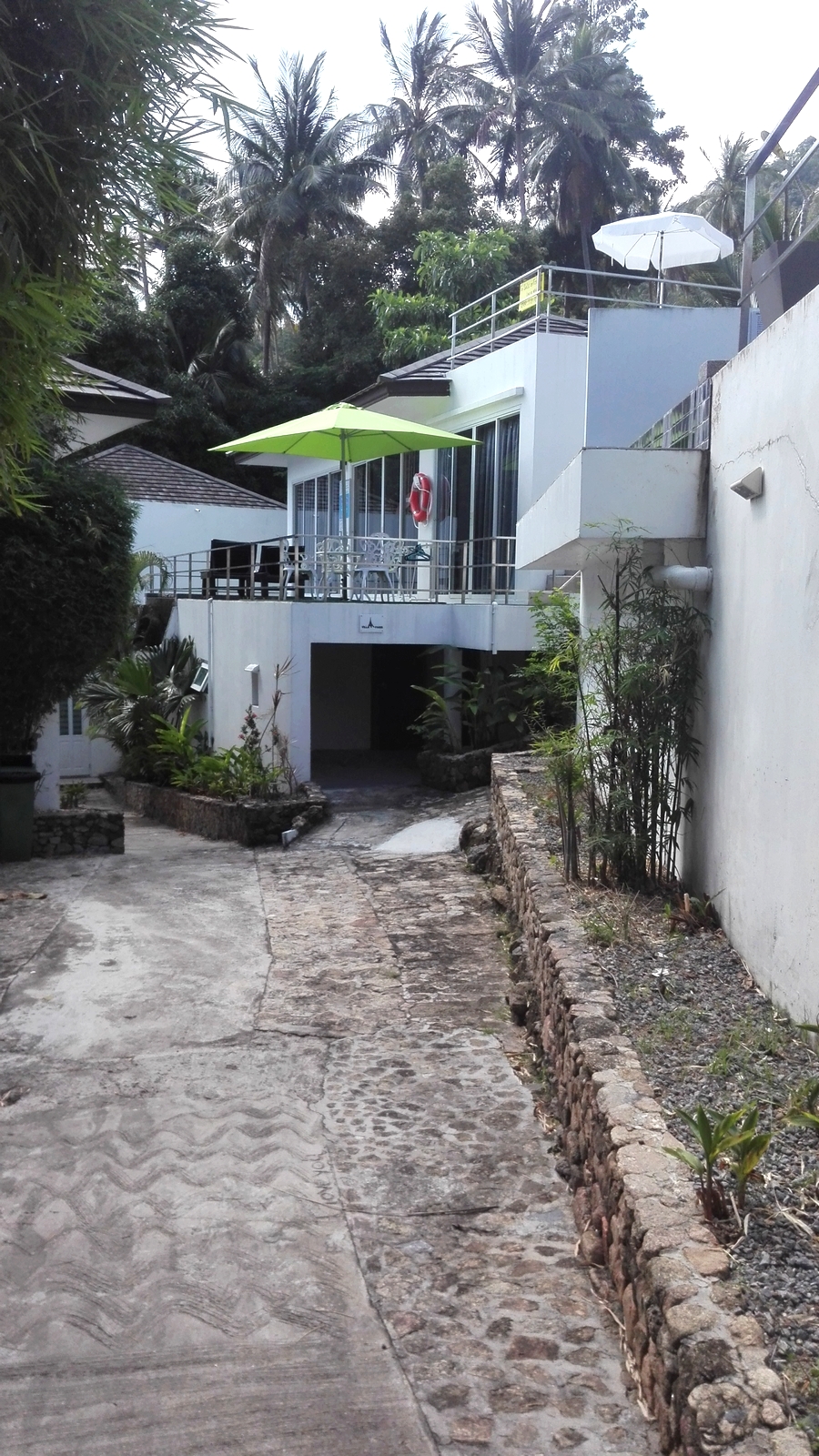 the exterior seen from the stone path on the terrace with swimming pool, parasol, garden furniture